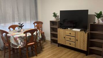 Un coin repas comprenant une table, des chaises, un téléviseur posé sur un meuble en bois et une plante en pot.