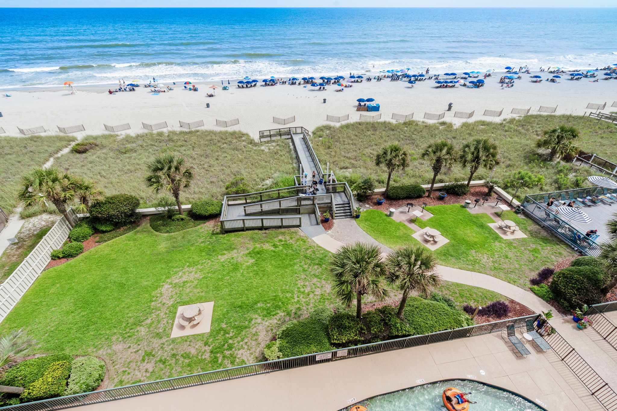A beach resort with a pool, a boardwalk, and a view of the ocean.