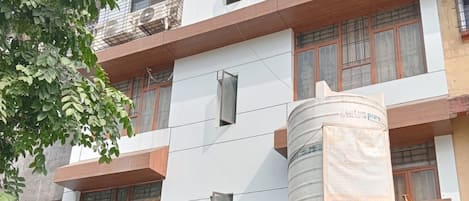 A multi-story residential building with a water tank, a balcony, and a gated entrance.