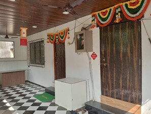 A room with a checkered floor, a ceiling fan, a wooden door, and a window with metal bars. - Rajtara Guest House (Navi Mumbai)