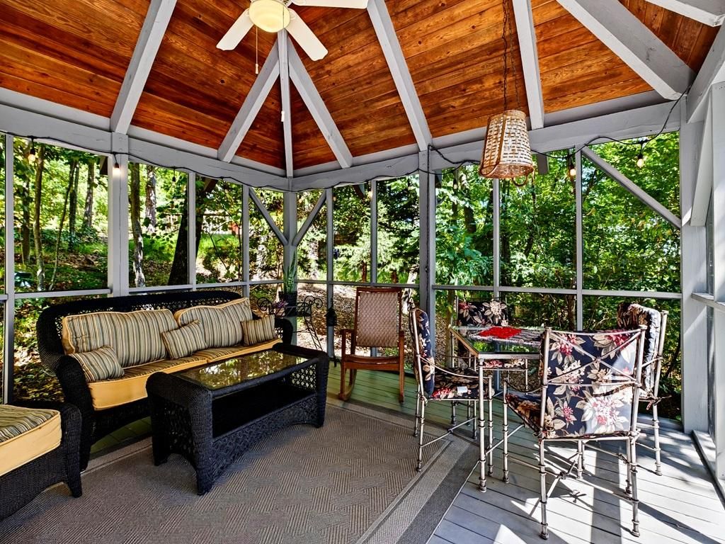 A covered outdoor seating area with a wooden ceiling, a sofa, chairs, and a table.