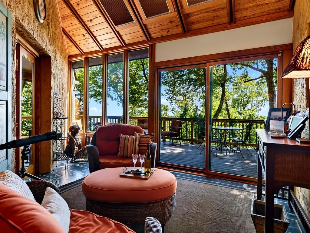 A cozy interior with a wooden ceiling, large windows, a comfortable seating area, and a view of the outdoors.