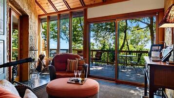 A cozy interior with a wooden ceiling, large windows, a comfortable seating area, and a view of the outdoors.