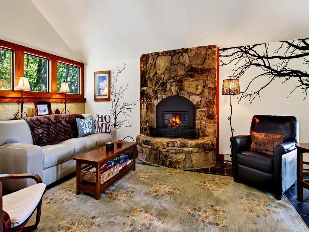 A living room with a stone fireplace, a sofa, a chair, and a rug.