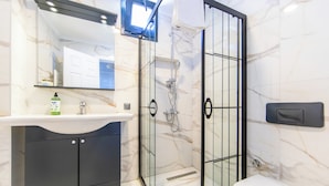 Une salle de bain avec un lavabo blanc, des meubles sombres, une douche en verre et des toilettes.