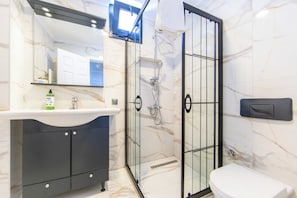A bathroom with a white sink, dark cabinets, a glass shower enclosure, and a toilet. - Mira villa 2 (Torba)