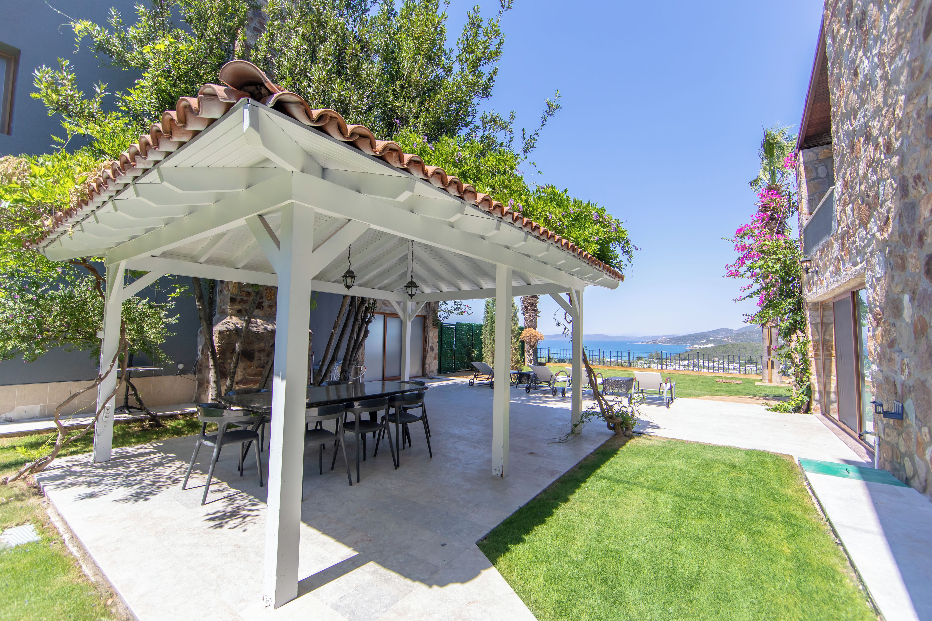 Un espacio de estar al aire libre cubierto con mesa y sillas, una pérgola con techo de tejas y vista al mar.