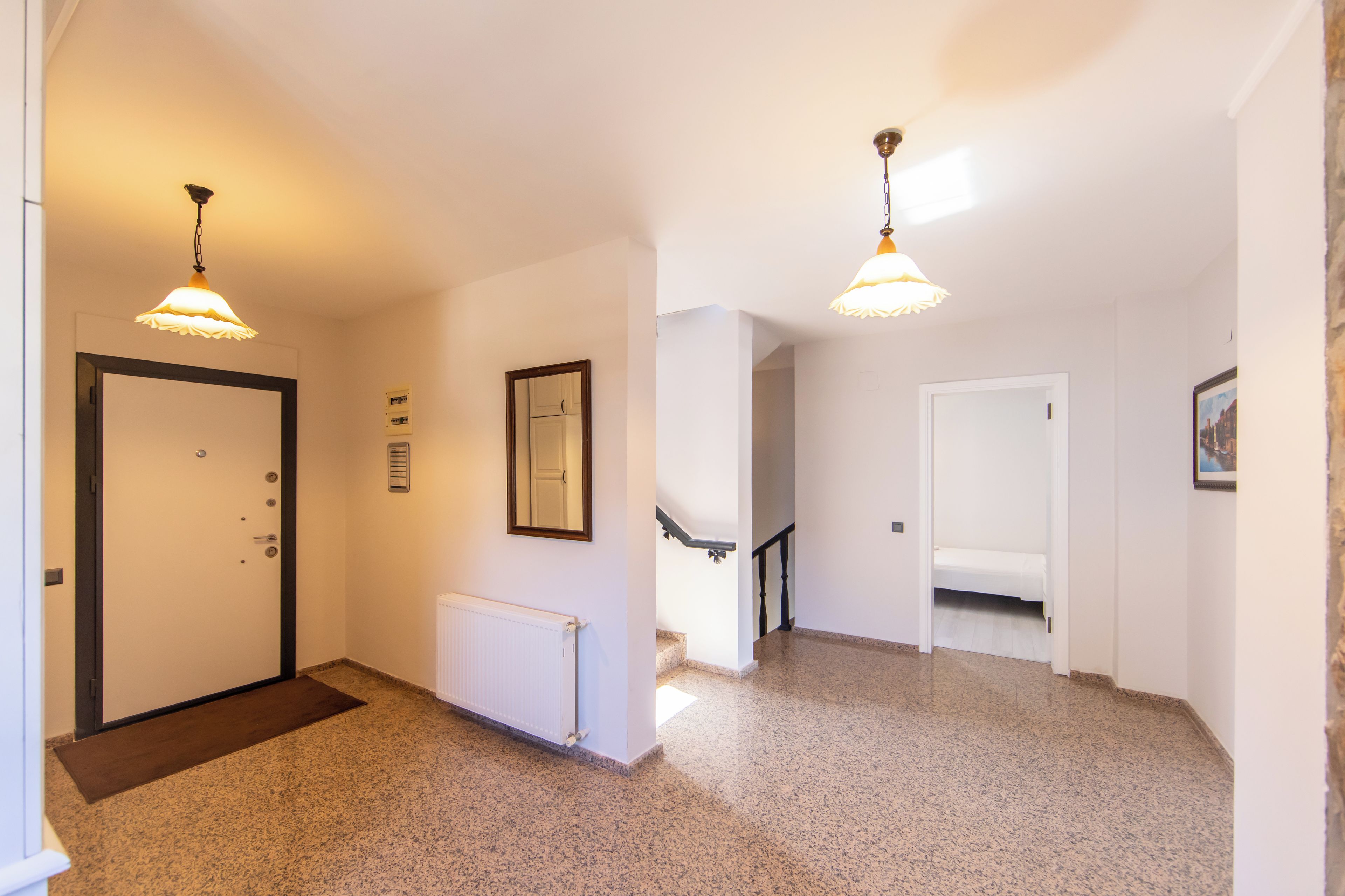 Un pasillo con una puerta, un radiador, un cuadro enmarco y una escalera que sube a otra habitación.