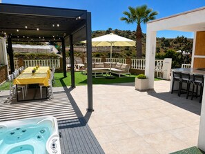 Eine überdachte Terrasse im Freien mit Whirlpool, Essbereich und Sitzgelegenheiten.
