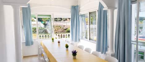A dining area with a long table, white chairs, and blue curtains.
