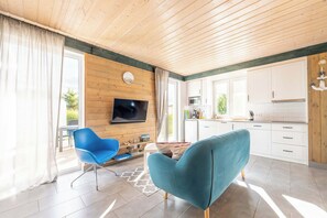 A modern kitchen with white cabinets, a flat-screen TV mounted on the wall, and a dining area with a blue chair. - Osada Rybacka - Seaside Cottage, Sauna included (Powiat wejherowski)