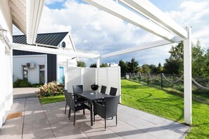 An outdoor patio with a table and chairs, a covered area, and a view of a green lawn and trees. - Osada Rybacka - Seaside Cottage, Sauna included (Powiat wejherowski)