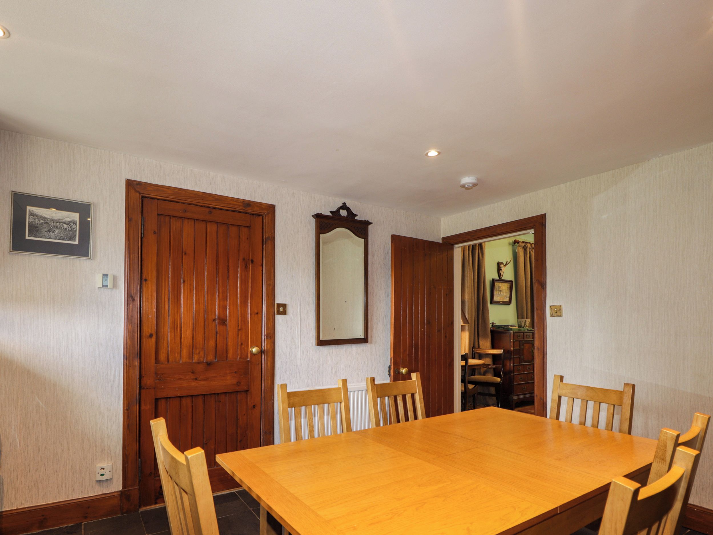 Un comedor con una mesa y sillas de madera, una puerta de madera y un espejo en la pared.