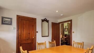 Un comedor con una mesa y sillas de madera, una puerta de madera y un espejo en la pared.