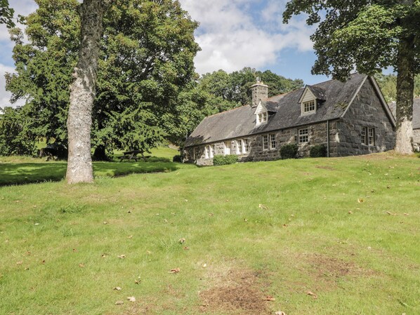 A stone building with a pitched roof, surrounded by a grassy field and trees. - Middle Lodge (Rogart)