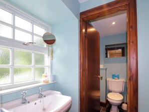 A bathroom with a white sink, a mirror, a toilet, and a window with a view of trees. - Middle Lodge (Rogart)