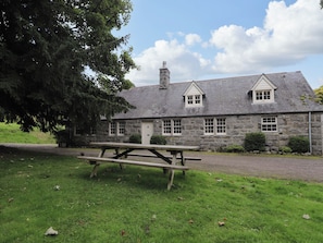 A stone building with a large tree in front, a picnic table, and a clear sky. - Middle Lodge (Rogart)