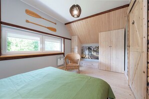 Een slaapkamer met een bed, een stoel, houten wanden, een raam en een deur.