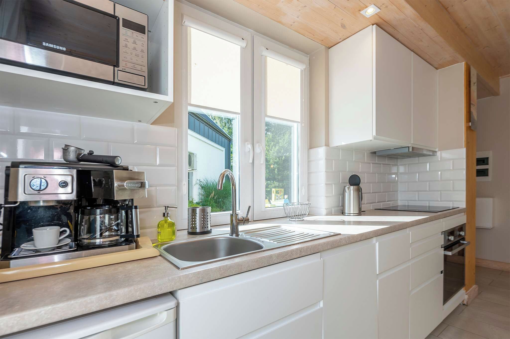 A modern kitchen with white cabinetry, a built-in microwave, a coffee machine, and a stainless steel sink.