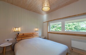 Ein Schlafzimmer mit einem hölzernen Kopfteil, einem großen Bett, Nachttischlampen, einem Fenster mit Blick und einer Heizung.