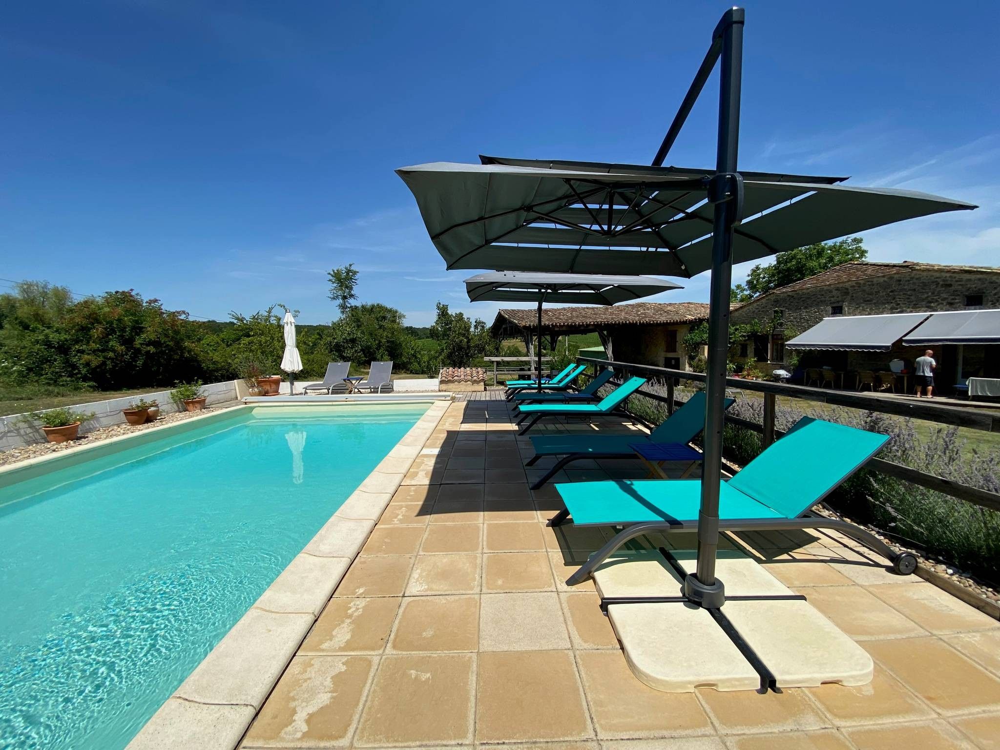 Piscina com espreguiçadeiras e guarda-sóis, ladeada por um terraço de pedra.