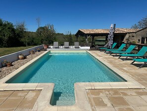 Una piscina rectangular con solárium enlosado, rodeada de sillones de descanso y plantas en macetas.