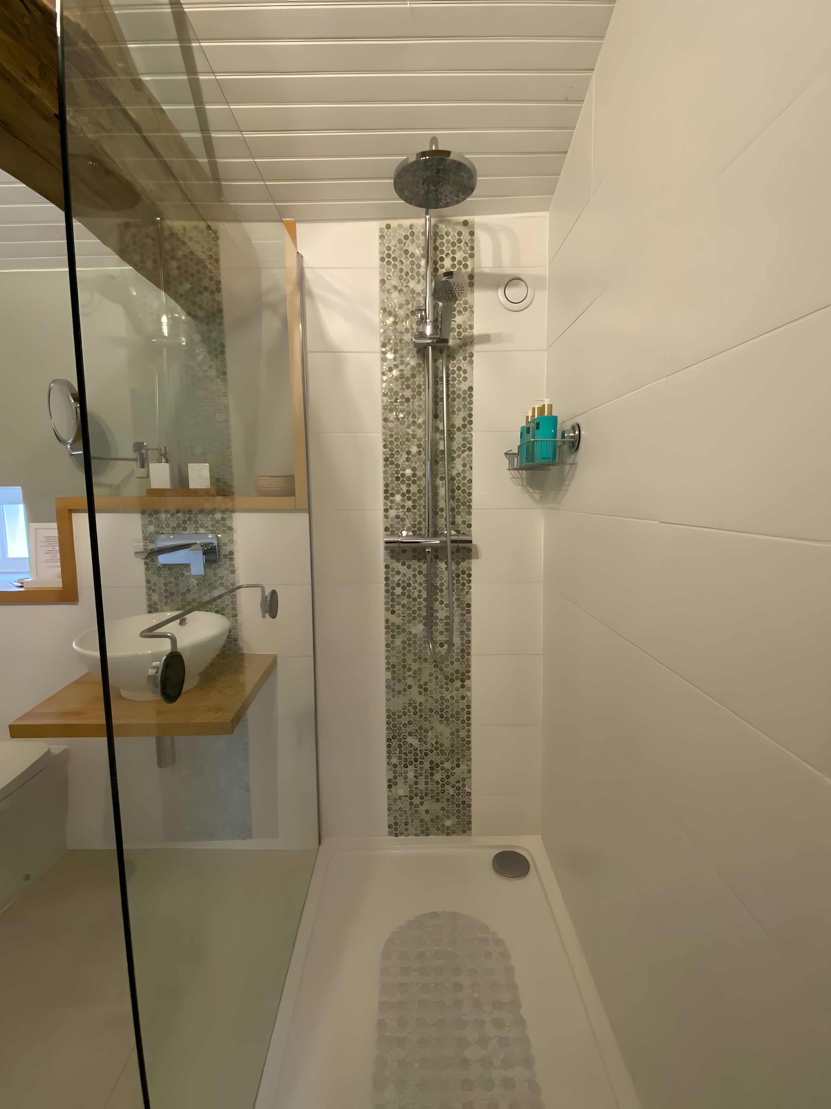 Un baño moderno con ducha envuelta en vidrio, un lavamanos blanco y un espejo.