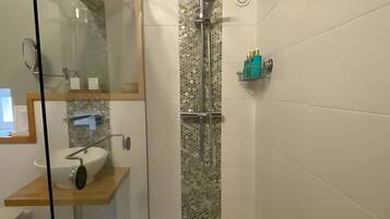 Un baño moderno con ducha envuelta en vidrio, un lavamanos blanco y un espejo.