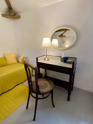 A room with a bed, a desk, a chair, a lamp, and a round mirror.