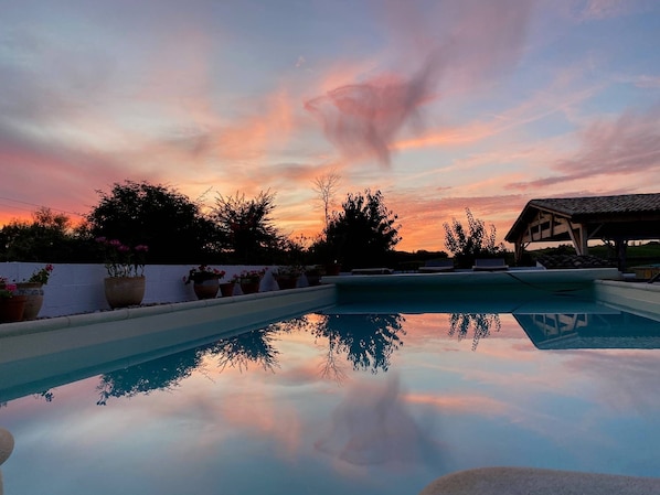 A swimming pool with a clear reflection of trees and a sunset sky.