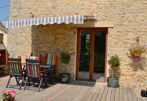 A stone building with a wooden deck, a covered seating area, and potted plants.