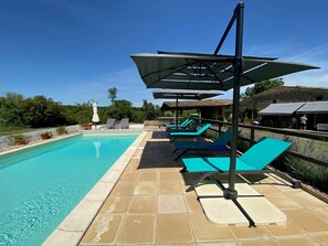 Ein Swimmingpool mit Liegestühlen und Sonnenschirmen, umgeben von einer Steinterrasse.
