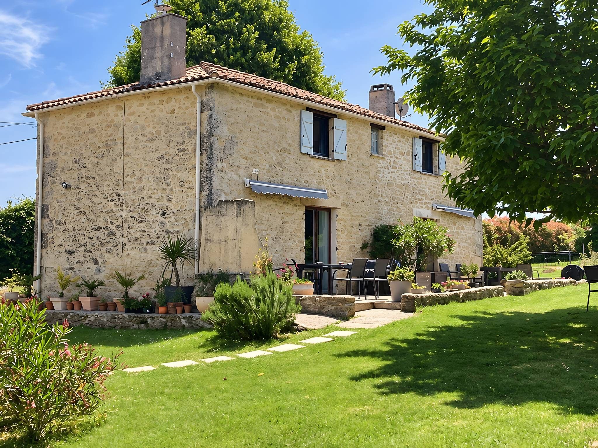 A stone house with a tiled roof, a small garden, and outdoor furniture.