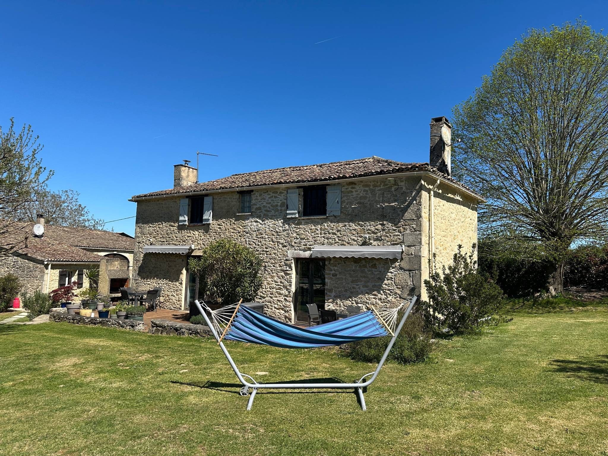 Une maison en pierre avec un jardin, un hamac et un ciel bleu azur.