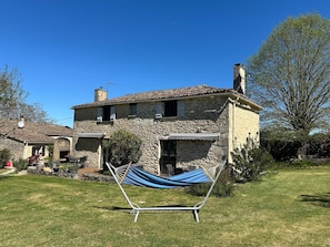 A stone house with a garden, a hammock, and a clear blue sky.