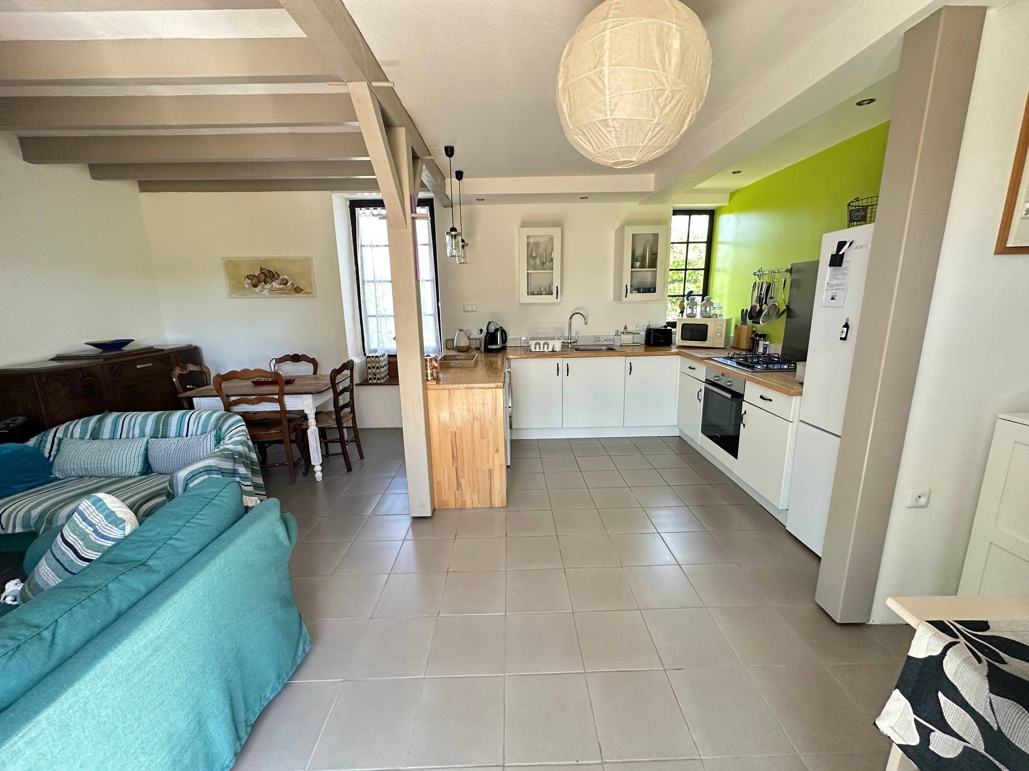 A modern kitchen with white cabinets, a central island, and a dining area with a sofa and chairs.