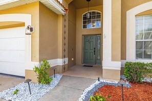 A residential building with a garage, a green door, a small porch with plants, and a window with a decorative light fixture. - 6BR Aviana Resort Escape | Pool, Spa + Game Room (Davenport)