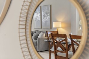 Ein Wohnzimmer mit einer Couch, einem Esstisch mit Stühlen, einer Lampe und zwei gerahmten Kunstwerken an der Wand.