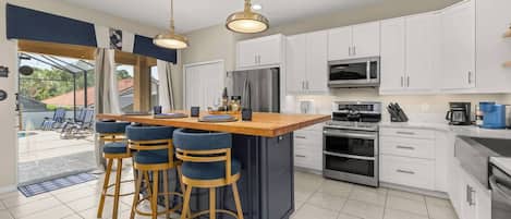Una cocina moderna con armarios blancos, una isla central con taburetes y electrodomésticos de acero inoxidable, además de iluminación colgante.