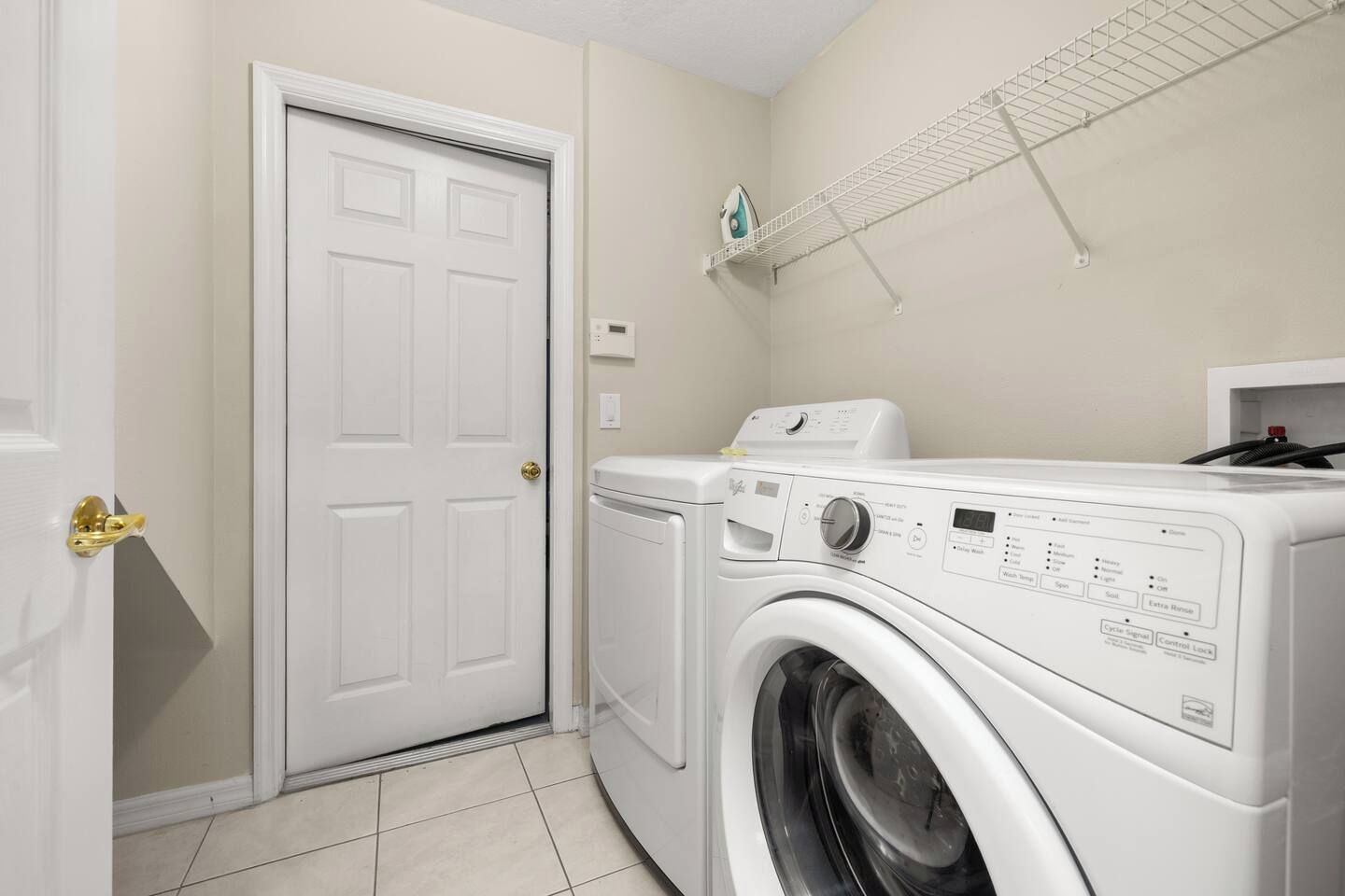 A laundry room with a front-loading washer and dryer, a drying rack, and a door with a brass handle.