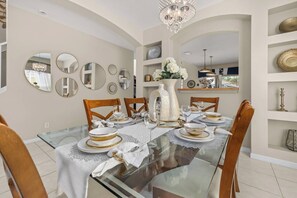 A dining room with a glass table, wooden chairs, and a chandelier. - 6BR Aviana Resort Escape | Pool, Spa + Game Room (Davenport)