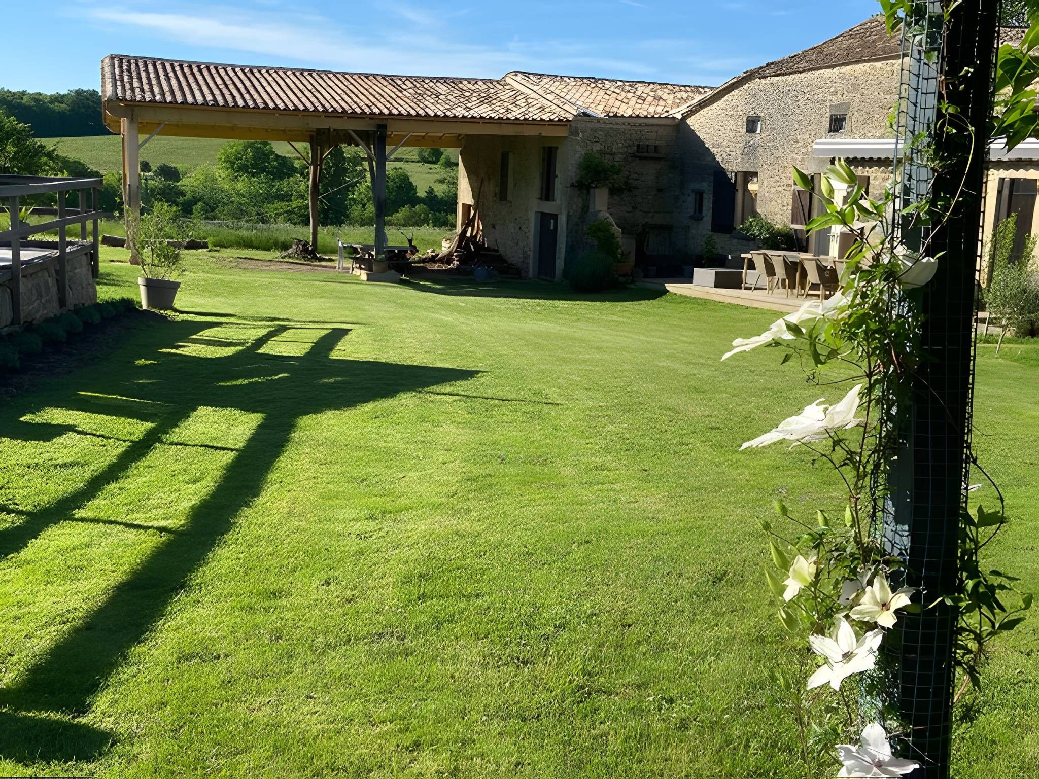 En välskött gräsmatta med en pergola, en byggnad i sten och en trädgårdsdel med vita blommor.