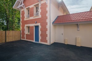 Un bâtiment à deux étages avec une façade en briques rouges, une porte bleue et un garage surmonté d’un toit recouvert de tuiles rouges.