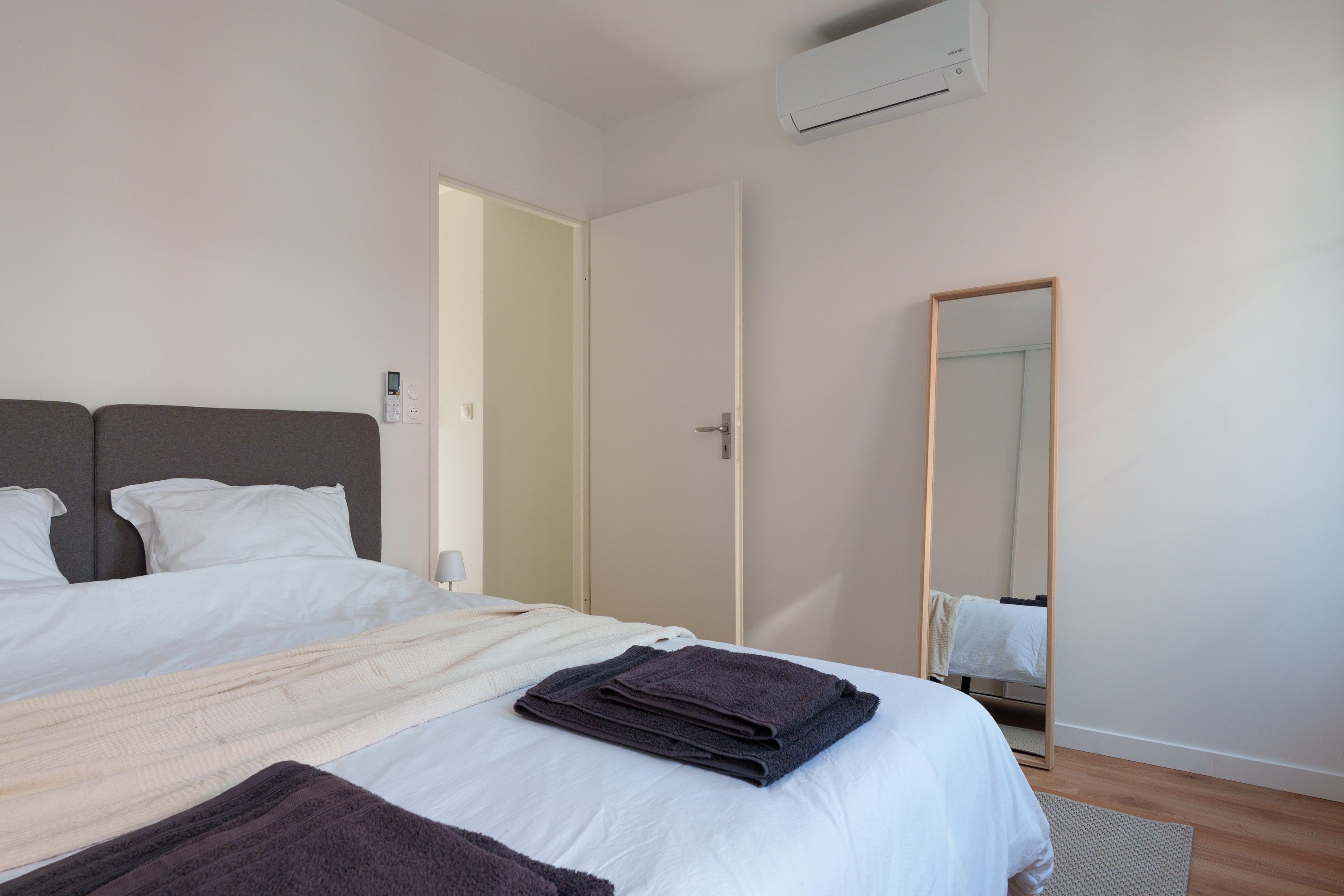 Een moderne slaapkamer met een bed, nachtkastje, spiegel en een airconditioning.