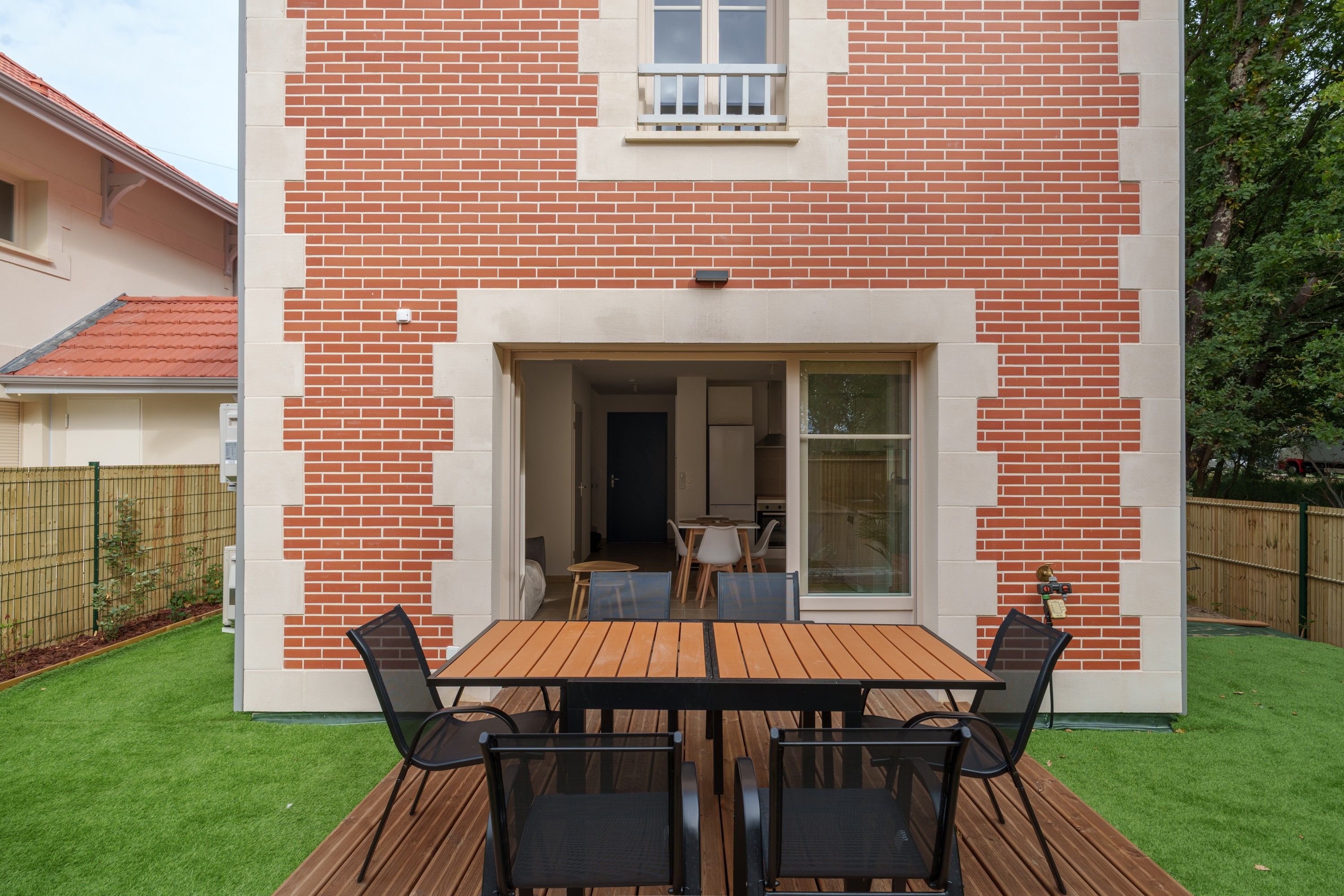 A modern house with a brick exterior, a wooden deck, and a glass door leading to an interior space.