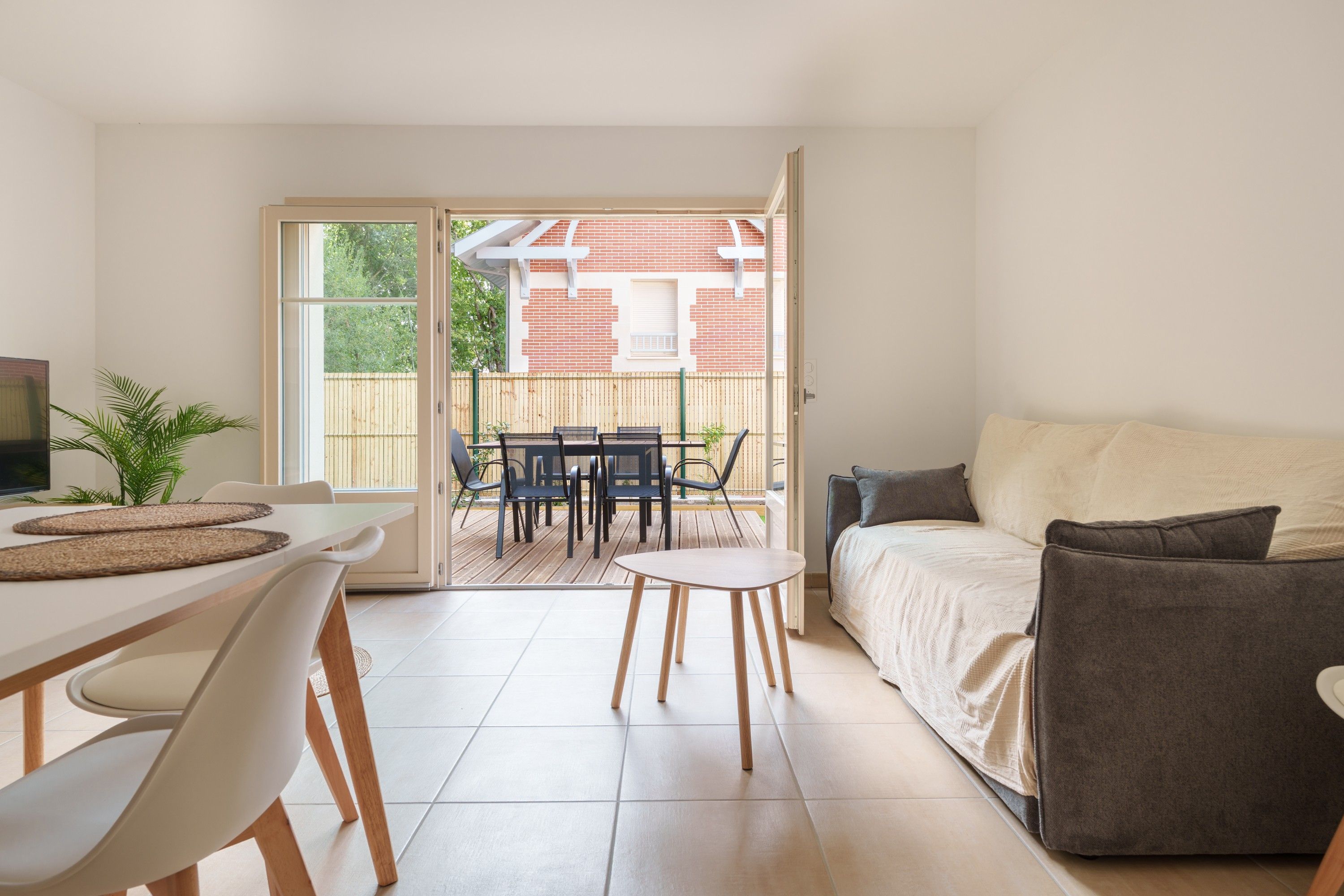 A modern living room with a sofa, a dining table with chairs, and a sliding glass door leading to an outdoor patio.