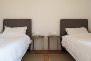 Une chambre d’hôtel avec deux lits simples, chacun recouvert d’une couette blanche et doté d’une petite table de chevet avec une lampe.