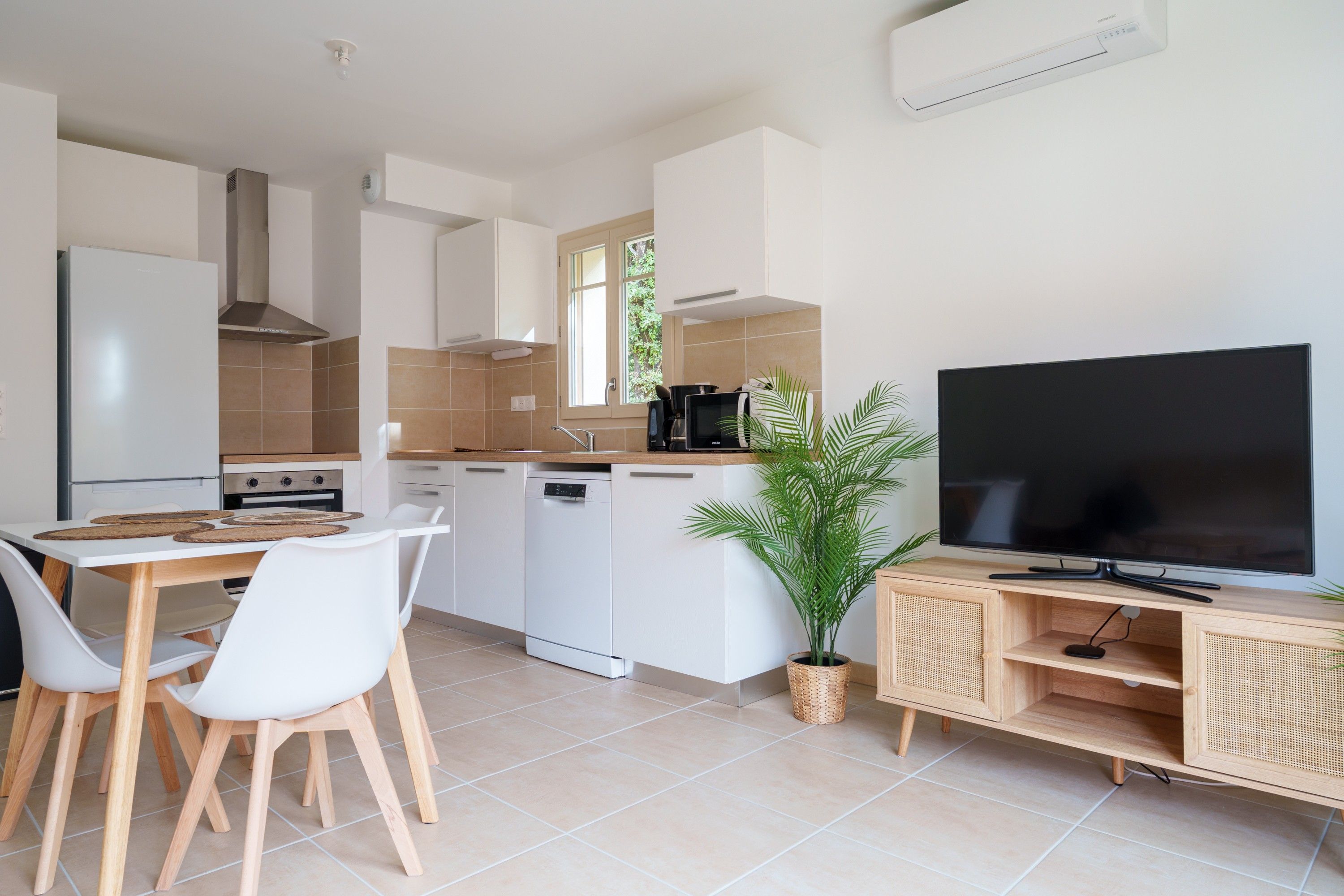 Een moderne keuken met witte kasten, een inbouwfornuis en een grote flatscreen televisie op een houten standaard.