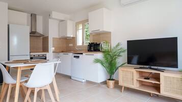 Een moderne keuken met witte kasten, een inbouwfornuis en een grote flatscreen televisie op een houten standaard.