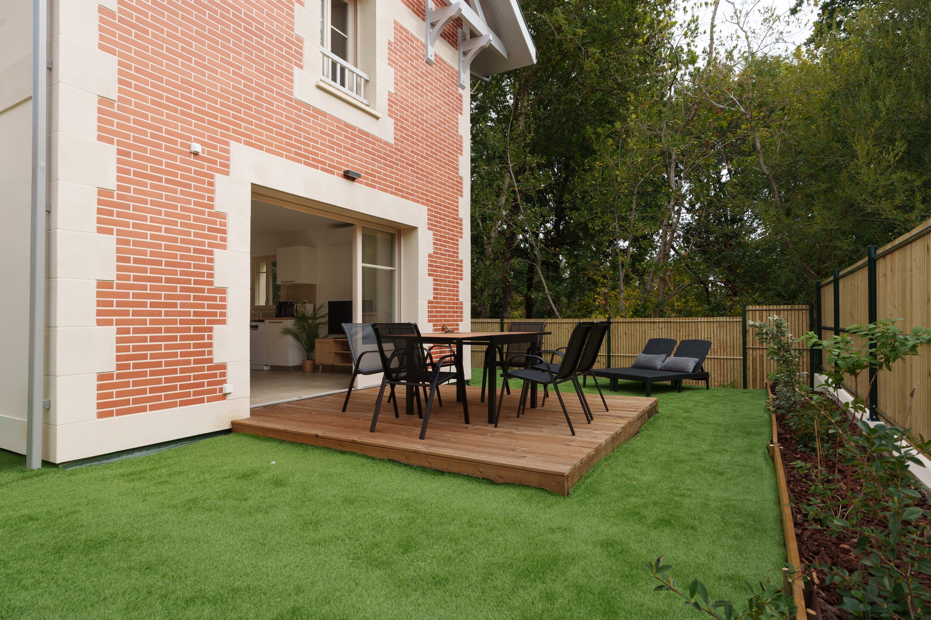 Une terrasse avec une table et des chaises, une plateforme en bois et une pelouse verdoyante.